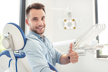 image of male patient sitting at dental chair at dentist office showing thumbs up
