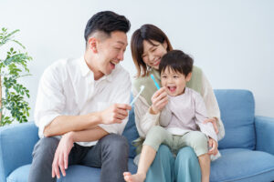 The image shows a family all holding toothbrushes and smiling to show the reasons to visit a dentist for the whole family